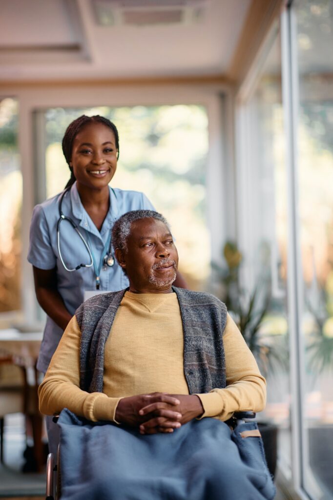 Pensive black senior in wheelchair and young nurse at residential care home.