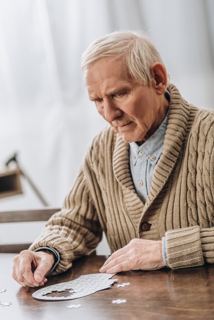 sad retired man with grey hair playing with puzzles at home